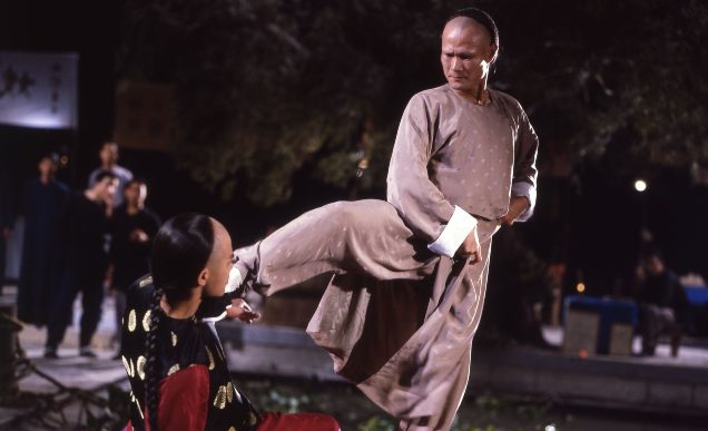 A man dressed in a grey robe looks down onto a man in black robes, holding him down with his outstretched foot.