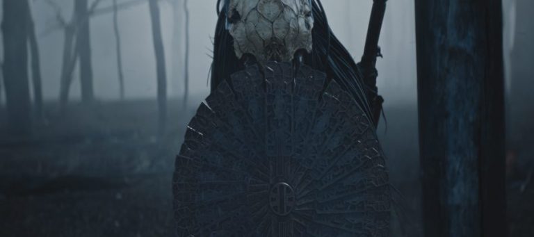 Screenshot from 'Prey'. The Predator hides behind a metallic shield in a ashen-laden forest.
