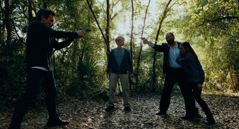 Three people pointing guns at each other in a still from Cover