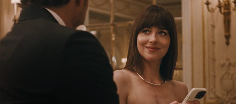Dakota Johnson smiles while holding her phone just about managing to resisit Pedro Pascal's advances in Materialists