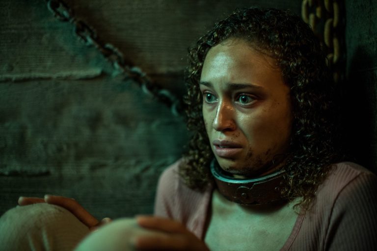 A woman with a chain collar around her neck in a scene from Your Host