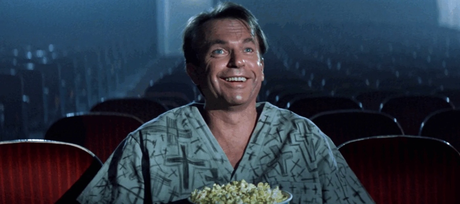 Sam Neill sits in his institution garb eating popcorn in John Carpenter's In the Mouth of Madness.