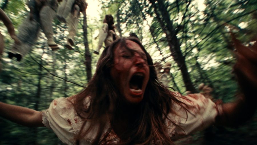 A woman covered in blood screaming while lying on a forest floor in a scene from Dolly