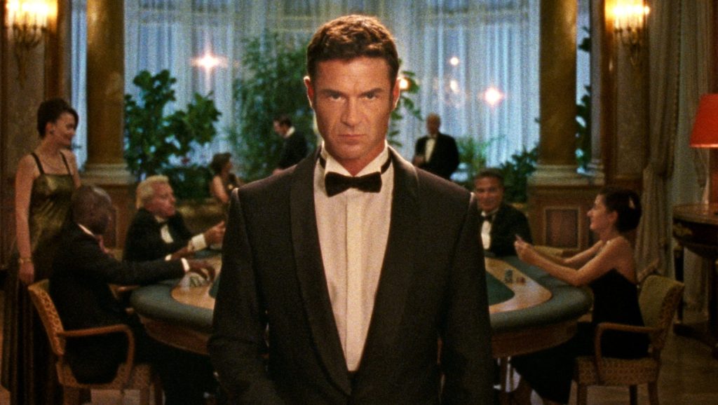 A man in a black tuxedo central in the scene staring at the camera in Reflection In A Dead Diamond