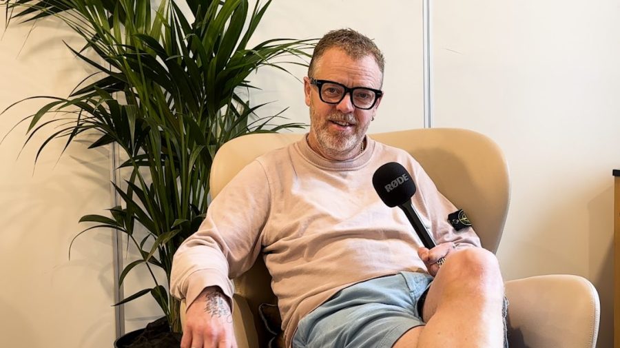 Director Paul Andrew Williams sat in a chair and holding a microphone as part of a recorded interview.