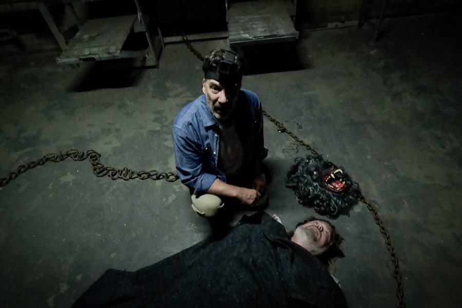 Mark Duplass as Josef standing over the body of a man next to a werewolf mask in a scene from The Creep Tapes.