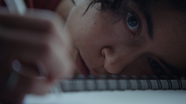 Tatiana Maslany as Liz in Keeper laying with her head on a notebook with a pen in her hand.