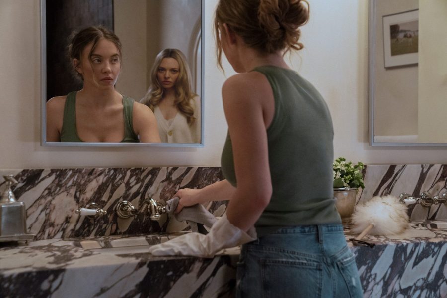 Sydney Sweeney looks into a mirror with a horrified look, as Amanda Seyfried is seen in the reflection standing behind her.